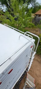 A trailer with a ladder positioned on top, set against a clear sky background.