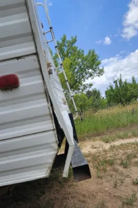 A white trailer featuring a ladder attached to its side, set against a neutral background.