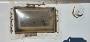 A window with a hole and a light bulb hanging nearby, illuminating the space with a warm glow.