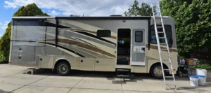 A motor home parked in a driveway beside a ladder leaning against it.